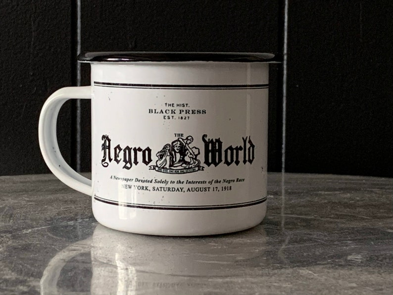 Peut inclure: Une tasse en &eacute;mail blanc avec un bord noir et une image en noir et blanc d'un titre de journal. Le titre est "The Negro World, A Newspaper Devoted Solely to the Interests of the Negro Race, New York, Saturday, August 17, 1918".