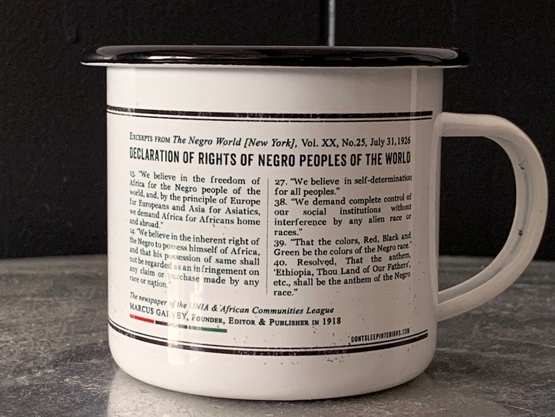 Peut inclure: Une tasse en &eacute;mail blanc avec un bord et une poign&eacute;e noirs. La tasse pr&eacute;sente une impression noir et blanc d'une d&eacute;claration des droits des peuples noirs du monde, publi&eacute;e en 1926 par le journal The Negro World. Le texte comprend la phrase "Ethiopie, Terre de nos P&egrave;res, etc., sera l'hymne de la race noire."