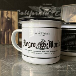 Peut inclure: Une tasse en &eacute;mail blanc avec un bord et une poign&eacute;e noirs. La tasse pr&eacute;sente une illustration en noir et blanc d'un titre de journal avec le texte "The Hist. Black Press Est. 1827 The Negro World A Newspaper Devoted Solely to the Interests of the Negro Race New York, Saturday, August 17, 1918."