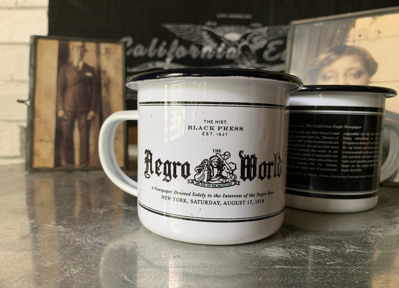 Peut inclure: Une tasse en &eacute;mail blanc avec un bord et une poign&eacute;e noirs. La tasse pr&eacute;sente une illustration en noir et blanc d'un titre de journal avec le texte "The Hist. Black Press Est. 1827 The Negro World A Newspaper Devoted Solely to the Interests of the Negro Race New York, Saturday, August 17, 1918."