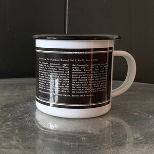 Puede incluir: Una taza de esmalte blanco con un borde y un asa negros. La taza tiene una imagen en blanco y negro de texto en el lateral. El texto dice "The Guardian (Boston), Vol. 1, No. 52, Nov. 1, 1902" e incluye un art&iacute;culo sobre el Memphis Commercial Appeal.