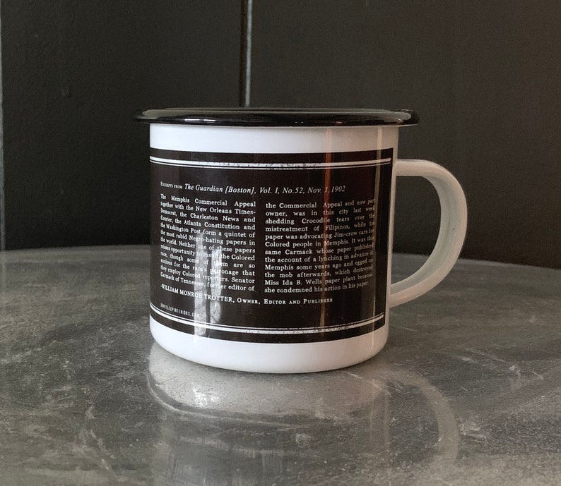 Puede incluir: Una taza de esmalte blanco con un borde y un asa negros. La taza tiene una imagen en blanco y negro de texto en el lateral. El texto dice "The Guardian (Boston), Vol. 1, No. 52, Nov. 1, 1902" e incluye un art&iacute;culo sobre el Memphis Commercial Appeal.