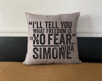 Può includere: Un cuscino grigio con testo nero che recita "Ti dirò cosa è la libertà per me NESSUNA PAURA." Nina Simone.
