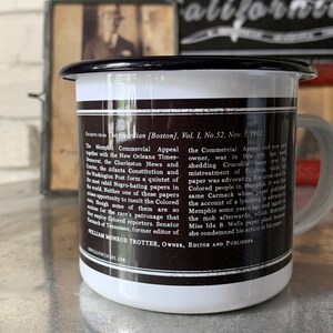 Puede incluir: Una taza de esmalte blanco con un borde y un asa negros. La taza tiene una imagen en blanco y negro de texto en el lateral. El texto dice "The Guardian [Boston], Vol. I, No. 52, Nov. 1, 1902" e incluye un extracto de un art&iacute;culo de peri&oacute;dico.