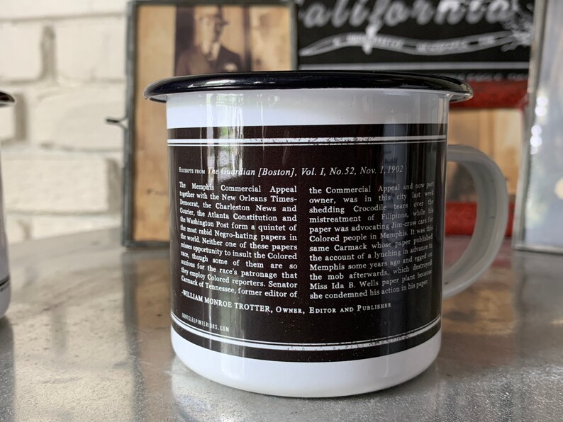 Puede incluir: Una taza de esmalte blanco con un borde y un asa negros. La taza tiene una imagen en blanco y negro de texto en el lateral. El texto dice "The Guardian [Boston], Vol. I, No. 52, Nov. 1, 1902" e incluye un extracto de un art&iacute;culo de peri&oacute;dico.