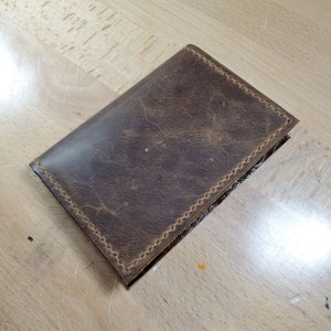 May include: A brown leather wallet with stitching around the edges.