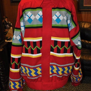 May include: A red button-up shirt with a geometric pattern in shades of blue, yellow, green, black, and white. The shirt has a collar and long sleeves.