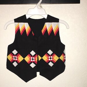 May include: A black vest with a geometric pattern in red, yellow, and white. The vest has a V-neck and is sleeveless.