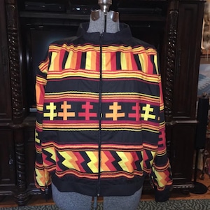May include: A black zip-up jacket with a colorful geometric pattern in red, yellow, and orange. The pattern features stripes, zigzags, and crosses.