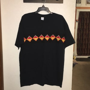May include: Black t-shirt with a colorful geometric design across the chest. The design features a row of red, orange, yellow, and blue diamonds.