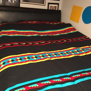 May include: A black bedspread with a colorful geometric pattern. The pattern features stripes of yellow, red, blue, and black.