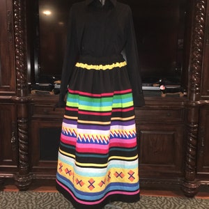 May include: A long black skirt with a colorful striped pattern. The skirt has a yellow waistband and a black top with a collar.
