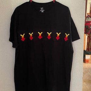 May include: Black t-shirt with a crew neck and short sleeves. The shirt features a series of red, yellow, and orange geometric shapes across the chest. The tag reads "[g] GEORGE".