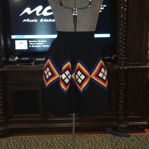 May include: Black skirt with a colorful geometric design. The skirt is displayed on a mannequin. The design features diamond shapes in red, yellow, white, and blue. The text "MC Music Choice JAZZ" is visible in the background.