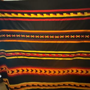 May include: Black blanket with horizontal bands of red, yellow, and orange geometric patterns. The blanket has a repeating design of diamonds and zigzags. The blanket is made of a soft material.