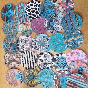 May include: A collection of 20 round coasters with various designs. The coasters feature a variety of patterns, including turquoise, black, white, pink, and brown. Some coasters have text, such as "Just a Small Town Girl" and "Southern Mama".