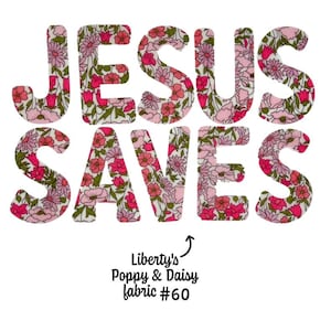 Peut inclure: Lettres en tissu floral épelant "JESUS SAUVE" en rose, rouge et vert. Le texte est placé sur un fond blanc. En dessous du texte se trouve la phrase "Liberty's Poppy & Daisy fabric #60".