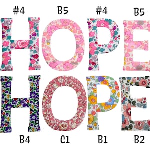May include: Eight fabric letters spelling the word HOPE twice, arranged in two rows. The letters feature various floral patterns in pink, purple, yellow, and blue. Each letter is labeled with a code such as #4, B5, B4, C1, B1, or B2.
