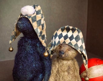 May include: Two handmade teddy bears wearing jester hats with black and white diamond patterns and gold bells. The bears are sitting on a brown surface with red and white balls.