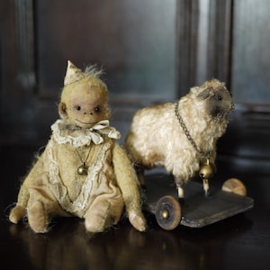 Puede incluir: Un mono de juguete vintage con un gorro de fiesta y un vestido de encaje, sentado junto a una oveja de juguete que tira de un carro de madera con ruedas.