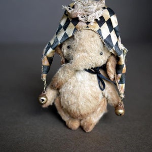 May include: A small, plush, beige elephant wearing a black and white checkered hat with gold bells. The hat has a ruffled trim.