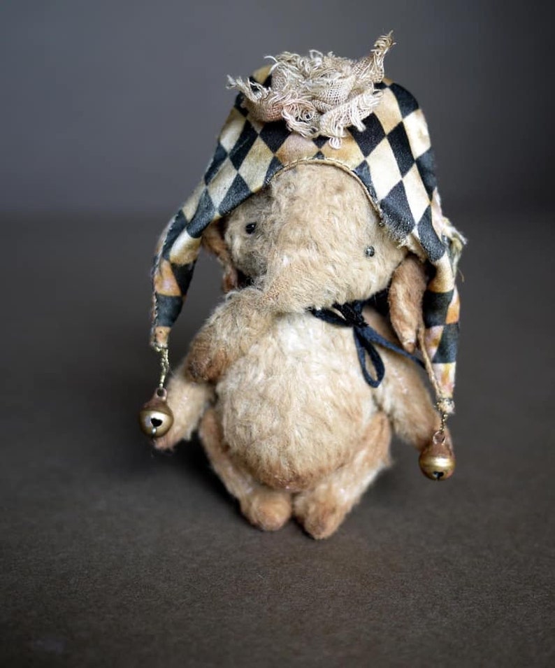 May include: A small, plush, beige elephant wearing a black and white checked hat with gold bells. The hat has a ruffled trim.