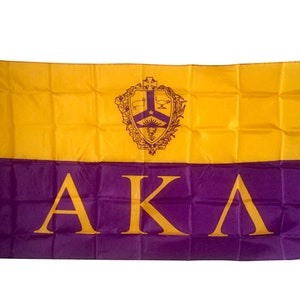 May include: A purple and gold flag with the letters "AKA" in purple on the bottom half and a crest with a star and other symbols on the top half.