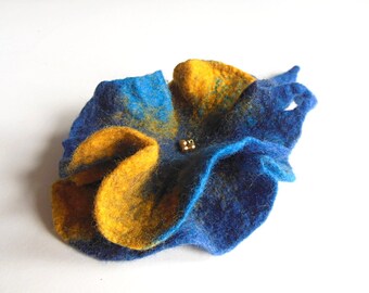 May include: A blue and yellow felt flower brooch with gold accents. The flower is made of felt and has a textured surface.