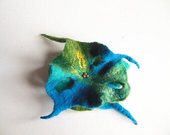 May include: A handmade felt flower brooch in shades of blue, green, and yellow. The brooch has a three-dimensional design with multiple petals and a small cluster of gold beads in the center. The brooch is approximately 4 inches in diameter.