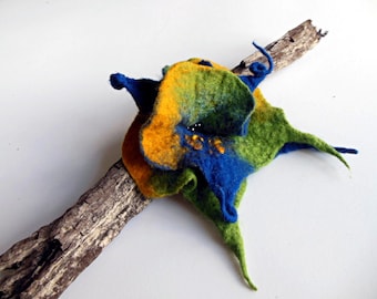 May include: A blue, green, and yellow felted flower with a twig attached to the back.