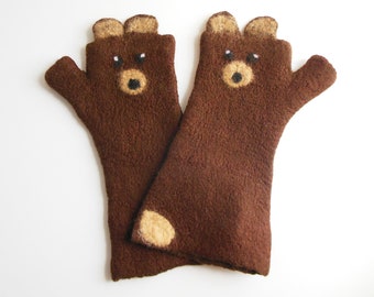 Può includere: Un paio di guanti senza dita marroni con un design a forma di muso d'orso. Ogni guanto presenta due piccole orecchie arrotondate in alto, due occhi bianchi e neri e un muso color sabbia con un naso nero. Un guanto ha una macchia circolare.