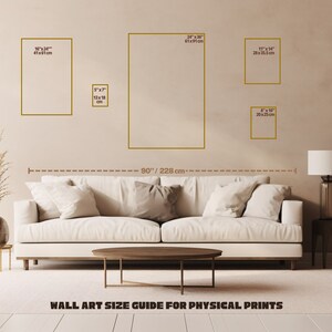 May include: A wall art size guide for physical prints with a white couch and a table in front of it. The guide shows different sizes of prints in inches and centimeters. The wall is beige and the floor is light brown.