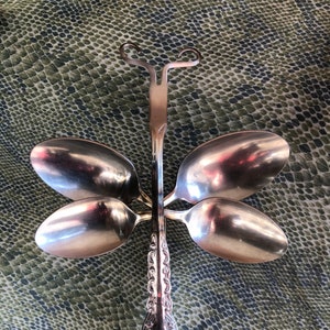 May include: A silver dragonfly sculpture made from spoons. The dragonfly has four wings and a long, slender body.