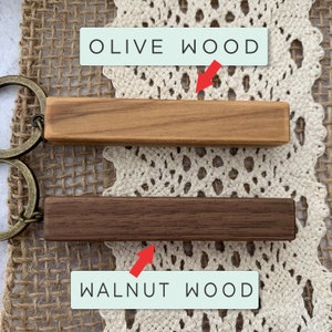 May include: Two wooden keychains, one is olive wood and the other is walnut wood. The keychains are both rectangular and have a natural wood finish.