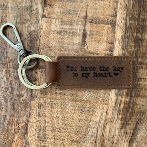 May include: Brown leather keychain with a silver key ring and a metal clasp. The leather tag has the text "You have the key to my heart." engraved on it.