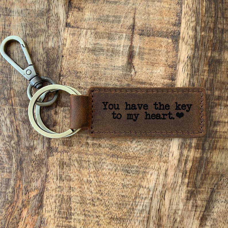 May include: Brown leather keychain with a silver key ring and a metal clasp. The leather tag has the text "You have the key to my heart." engraved on it.
