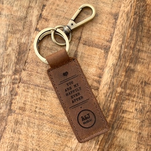 May include: A brown leather keychain with a metal ring and clasp. The keychain has the text "You are my happily ever after" and "A&J 12-15-18" engraved on it.