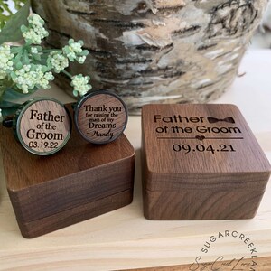 May include: Wooden box with a bow tie design and the text "Father of the Groom" and the date "09.04.21". The box is open and contains two wooden cufflinks. One cufflink has the text "Father of the Groom" and the date "03.19.22". The other cufflink has the text "Thank you for raising the man of my Dreams Mandy".