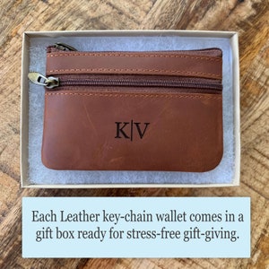 May include: A brown leather key chain wallet with a zipper closure and the initials "K|V" engraved on the front. The wallet is in a white gift box.