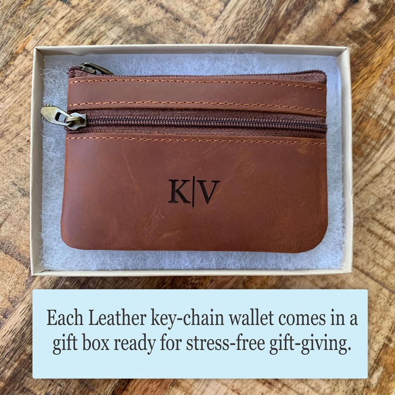May include: A brown leather key chain wallet with a zipper closure and the initials "K|V" engraved on the front. The wallet is in a white gift box.