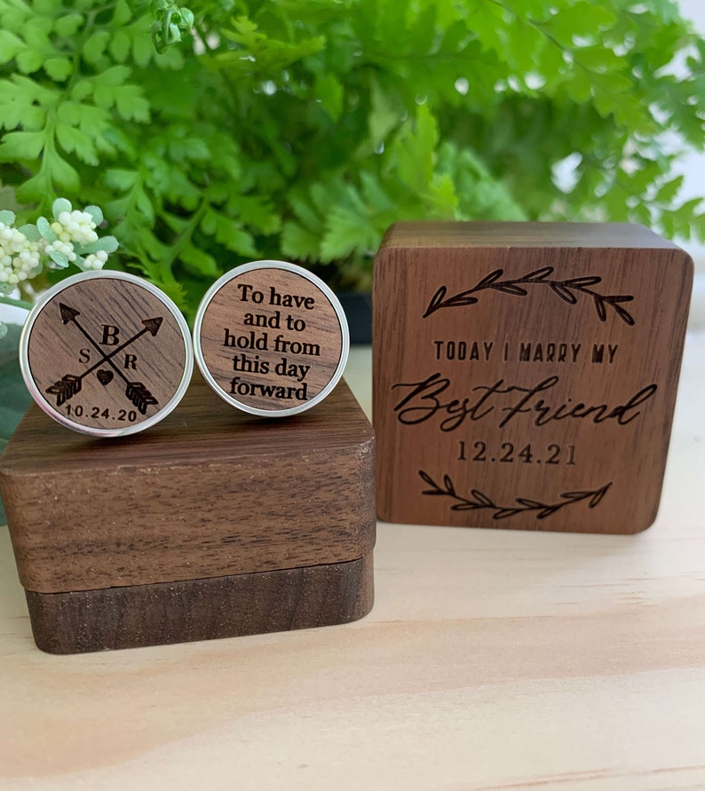 May include: A wooden box with a lid engraved with the text "Today I marry my Best Friend 12.24.21". The box contains two wooden cufflinks with silver accents. One cufflink is engraved with the text "To have and to hold from this day forward". The other cufflink is engraved with the text "S B R 10.24.20" and two arrows.