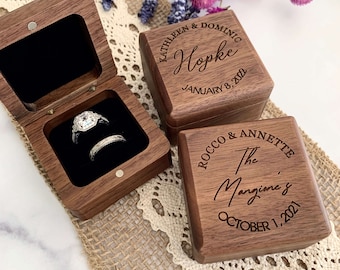May include: Two wooden ring boxes with engraved text. The top box has the text "KATHLEEN & DOMINIC Hopke JANUARY 8, 2022". The bottom box has the text "ROCCO & ANNETTE The Margine's OCTOBER 1, 2021".