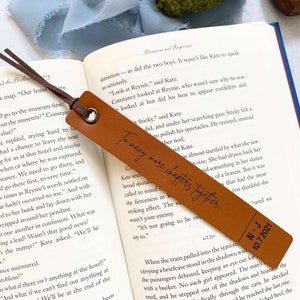 Peut inclure: Un marque-page en cuir marron avec le texte "To many more chapters together" et la date "10.7.2021" en lettres dor&eacute;es. Le marque-page est pos&eacute; sur un livre avec du texte sur un mus&eacute;e.