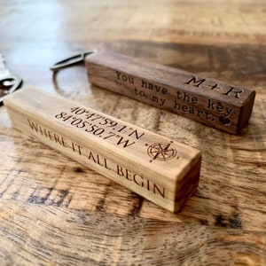 May include: Two wooden keychains with engraved text. The first keychain is brown and reads "M+R You have the key to my heart." The second keychain is light brown and reads "40&deg;47'59.1"N 84&deg;05'50.7"W WHERE IT ALL BEGIN".