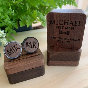 May include: Two wooden boxes with engraved text. The top box has the text "MICHAEL BEST MAN" and "CHRISTOPHER + ABIGAIL 02.12.22". The bottom box has the text "MK" engraved on two cufflinks. The text "Jason Will you be my groomsman?" is also engraved on the box.