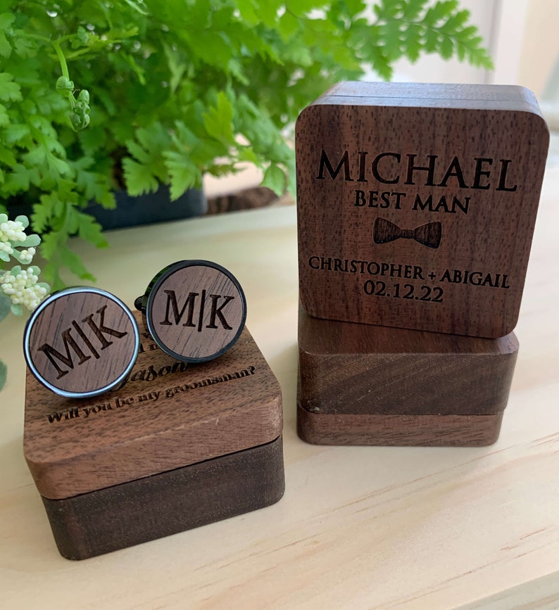 May include: Two wooden boxes with engraved text. The top box has the text "MICHAEL BEST MAN" and "CHRISTOPHER + ABIGAIL 02.12.22". The bottom box has the text "MK" engraved on two cufflinks. The text "Jason Will you be my groomsman?" is also engraved on the box.