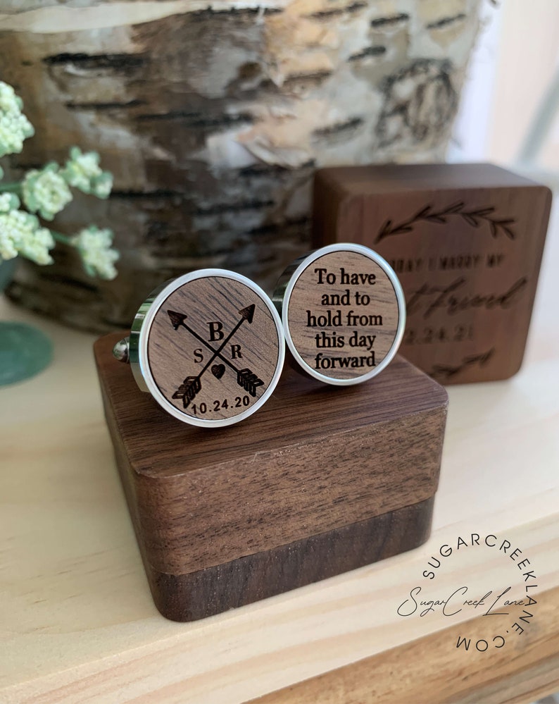 May include: Wooden cufflinks in a walnut box. One cufflink has the initials "S" and "R" with a heart and arrows. The other cufflink has the text "To have and to hold from this day forward".