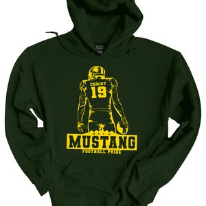 May include: A dark green hooded sweatshirt with a yellow silhouette of a football player wearing a jersey with the name "CHRIST" and the number "19" on the back. The text "MUSTANG FOOTBALL PRIDE" is printed below the player.