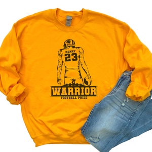 May include: Yellow sweatshirt with a black silhouette of a football player wearing the number 23 and the name "HENRY" above the number. The text "WARRIOR FOOTBALL PRIDE" is below the player.