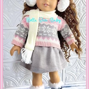 May include: A doll wearing a grey and pink sweater with a white snowflake pattern, a grey skirt, a white scarf, and grey boots with white fur trim. The doll has brown curly hair and is wearing a white earmuff headband.